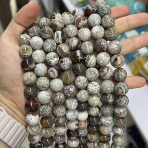 May include: A strand of round gemstone beads in shades of gray, brown, and cream. The beads have a marbled appearance, with swirling patterns and variations in color. The beads are approximately 0.4 inches in diameter, suitable for jewelry making.