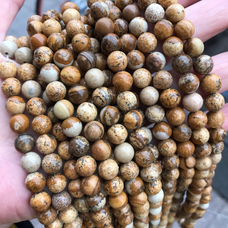 May include: A strand of brown, beige, and white jasper beads. The beads are round and have a speckled pattern.