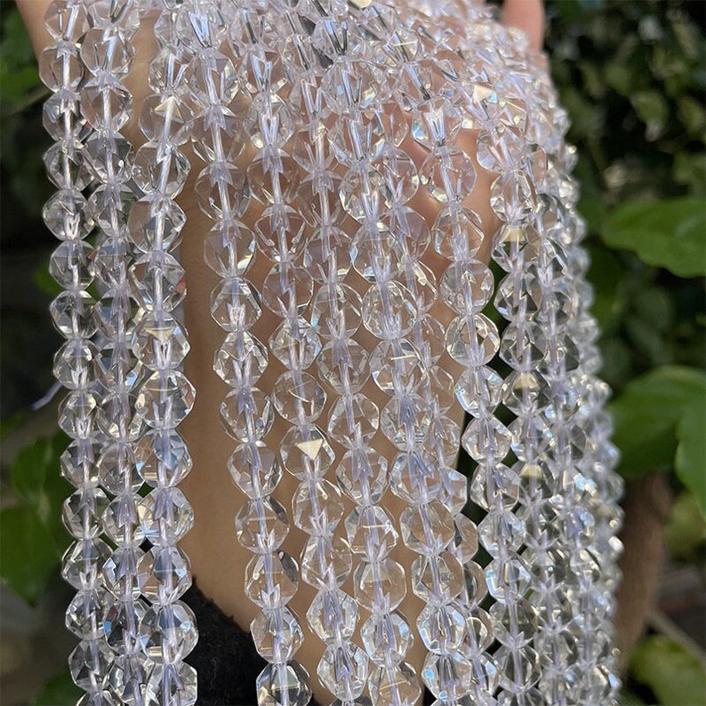 May include: A strand of clear faceted crystal beads. The beads are strung on a clear thread and are arranged in a cascading pattern. The beads are all the same size and shape, and they have a smooth, polished finish.