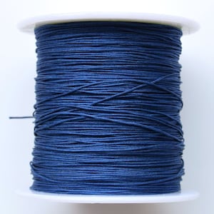 Puede incluir: Una bobina de cord&oacute;n el&aacute;stico azul oscuro, enrollada apretadamente en una bobina de pl&aacute;stico blanco.