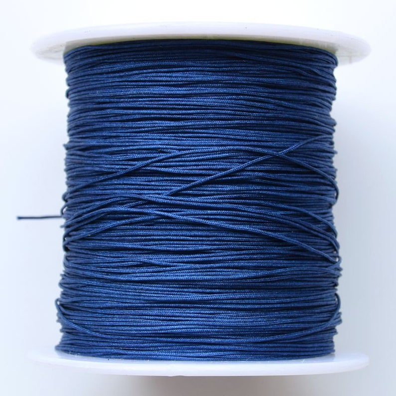 Puede incluir: Una bobina de cord&oacute;n el&aacute;stico azul oscuro, enrollada apretadamente en una bobina de pl&aacute;stico blanco.