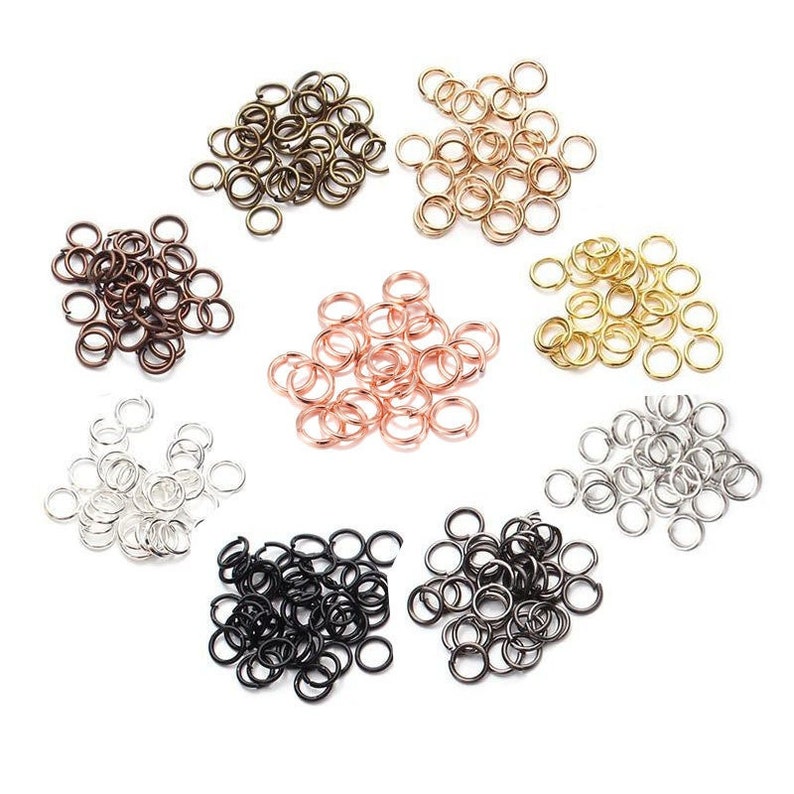 Peut inclure: Un assortiment de anneaux de jonction de diff&eacute;rentes finitions m&eacute;talliques, argent, or, bronze, cuivre et noir. Ces petits anneaux circulaires sont utilis&eacute;s pour la fabrication de bijoux et l'artisanat. Les anneaux sont dispers&eacute;s sur une surface blanche.