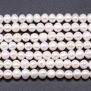 May include: A strand of white freshwater pearls, each pearl is round and smooth. The pearls are arranged in a row, with the top row slightly overlapping the bottom row.