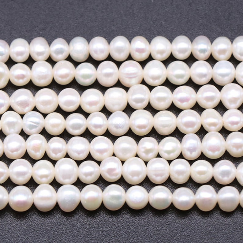 May include: A strand of white freshwater pearls, each pearl is round and smooth. The pearls are arranged in a row, with the top row slightly overlapping the bottom row.