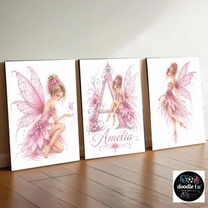 Könnte beinhalten: Drei gerahmte Feen-Kunstdrucke. Die Drucke zeigen Illustrationen von Feen in rosa Kleidern und Flügeln. Ein Druck enthält den Namen "Amelia" und den Buchstaben "A". Die Kunst ist auf weißem Hintergrund.