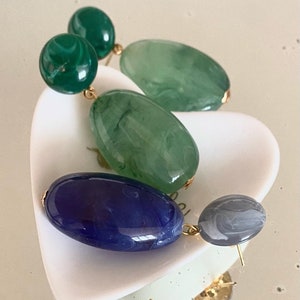 May include: A pair of dangle earrings featuring three oval-shaped beads in green, blue and grey. The beads have a marbled effect.