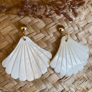 Peut inclure: Une paire de boucles d'oreilles en forme d'éventail en coquille blanche avec des accents dorés. Les boucles d'oreilles ont un design délicat et complexe.