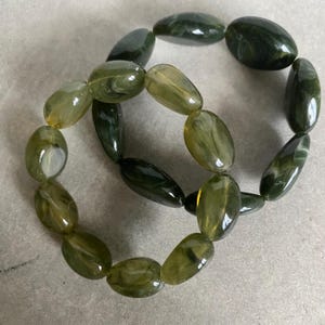 May include: Two green and yellow oval-shaped beaded bracelets. The bracelets are made of natural stone and are stacked on top of each other.