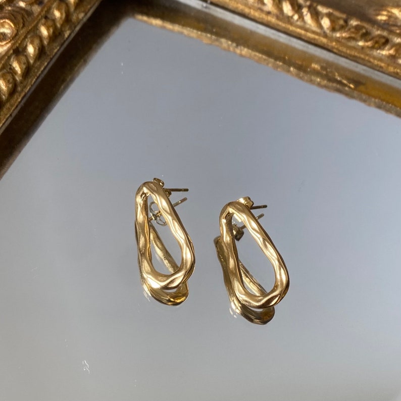May include: A pair of gold-toned, textured, open-circle earrings. The earrings are simple and modern in design.
