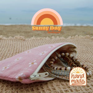 May include: A pink floral print pouch with a white zipper, filled with beaded bracelets. The pouch is open, revealing the jewelry. The image includes a "Sunny Day" logo and a "hand made" sticker.