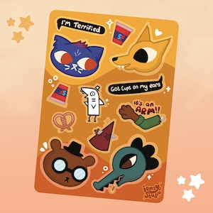 May include: A sticker sheet featuring cartoon illustrations in various colors. The sheet includes a blue cat face with the text "I'm Terrified", a yellow fox head, a white shark-like character, a brown bear with glasses, and other quirky designs. The text "Got Cups on my ears" is also present.