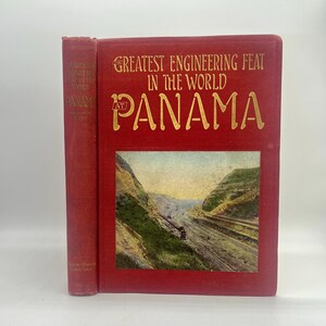 May include: A vintage red book titled "Greatest Engineering Feat in the World at Panama" with gold lettering. The cover features a color image of the Panama Canal. The spine of the book is also red.