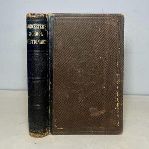 May include: A vintage, brown leather-bound book with the title "Worcester's School Dictionary" embossed on the spine. The front cover features a decorative design with the word "Dictionary" embossed in the center.
