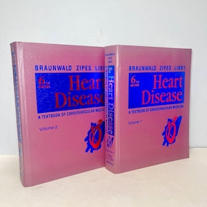 Puede incluir: Dos libros de tapa dura de color rosa titulados "Braunwald Zipes Libby 6ª edición Enfermedad cardíaca Un libro de texto de medicina cardiovascular" con letras azules y rojas. El libro de la izquierda es el Volumen 2 y el libro de la derecha es el Volumen 1.