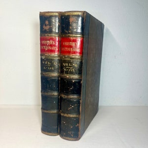 May include: Two antique Webster's Dictionary books. The spines are black with red labels that read "Webster's Dictionary". Volume I and II are visible. The books have gold accents and are in good condition.