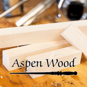 May include: Close-up of several light-colored Aspen wood blocks, with the text "Aspen Wood" in a black, stylized font. A black wand is at the bottom. The wood is on a wooden surface.