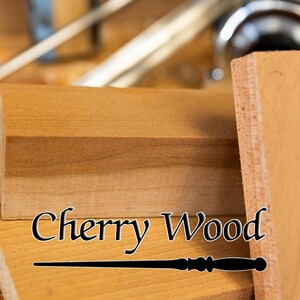 May include: Close-up of cherry wood blocks with the text "Cherry Wood" in a stylized font. The wood has a warm, reddish-brown hue, and the grain is visible. A dark-colored wand is at the bottom of the image.