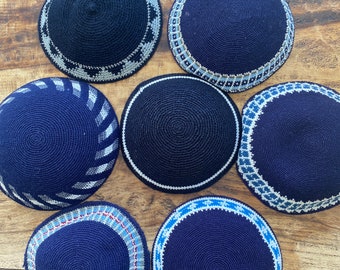 May include: Six blue knitted kippahs with different white and blue patterned borders.