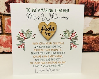 Puede incluir: Una tarjeta de felicitación blanca para un profesor con un corazón de madera con la etiqueta Pocket Hug. La tarjeta incluye el texto To My Amazing Teacher Mrs Williams, un poema navideño y la firma Love Rosie xx, decorada con acebo.
