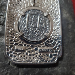 May include: A silver pendant featuring a replica of a Spanish silver coin with the inscription "8 Reales" and the year "1780". The pendant is marked "925" and "J. Spirit &copy;".