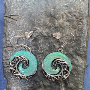 May include: A pair of silver earrings with a turquoise blue swirl design. The earrings are made of metal and have a delicate, intricate design.