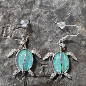 May include: A pair of silver turtle earrings with iridescent blue and green opal stones.