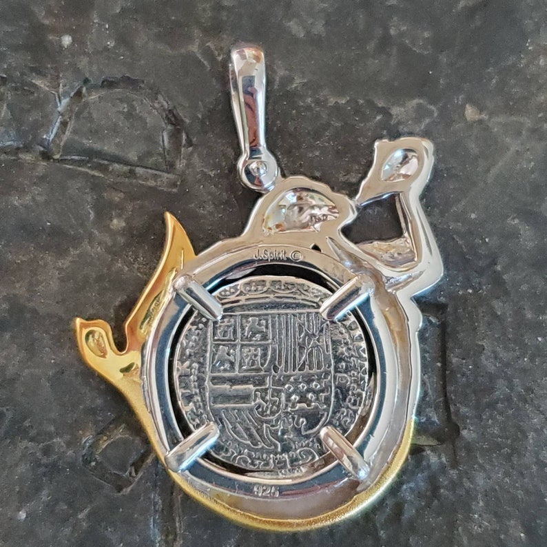 May include: Silver and gold tone pendant featuring a detailed replica of a Spanish coin with the inscription "J. Spirit C" on the back.