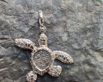 May include: Silver turtle pendant with a detailed design. The turtle's shell is a replica of a Spanish coin with a cross and other markings.