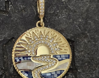 May include: A gold oval pendant with a sun and a river design. The sun is made of white rhinestones and the river is made of blue and white enamel. The pendant has a gold bail.