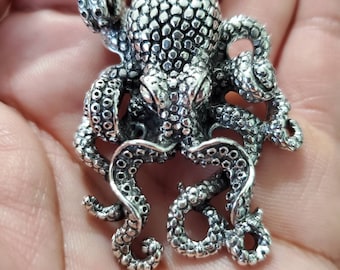 May include: A silver octopus pendant with a detailed, textured design. The octopus has eight tentacles and a textured body.