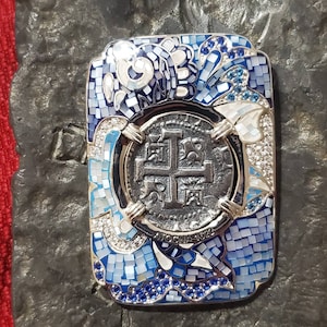 May include: A silver pendant with a blue and white enamel design. The pendant features a cross and the text "Ave Maria 1622".