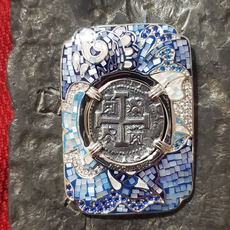 May include: A silver pendant with a blue and white enamel design. The pendant features a cross and the text "Ave Maria 1622".