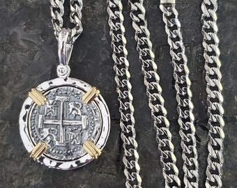 May include: Silver necklace with a round pendant featuring a silver coin with a cross design and gold accents. The necklace is made of a silver curb chain.