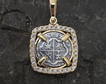 May include: A silver coin pendant with a gold frame set with clear round stones. The coin features a design of four crosses.