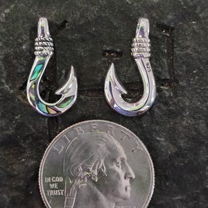 May include: Two silver fish hook pendants with abalone shell inlay. The hooks are about the size of a US quarter.