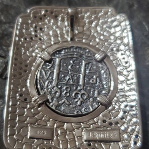 May include: A silver pendant featuring a detailed replica of a silver coin with the inscription "J. Spirit&copy;" and "925" on the back. The pendant is set in a textured silver frame.