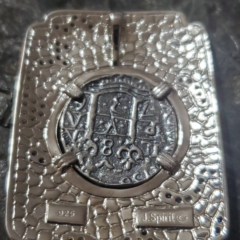 May include: A silver pendant featuring a detailed replica of a silver coin with the inscription "J. Spirit&copy;" and "925" on the back. The pendant is set in a textured silver frame.