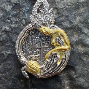 May include: A silver and gold pendant featuring a mermaid with a crown of jewels, a turtle, and a silver coin with a cross design.