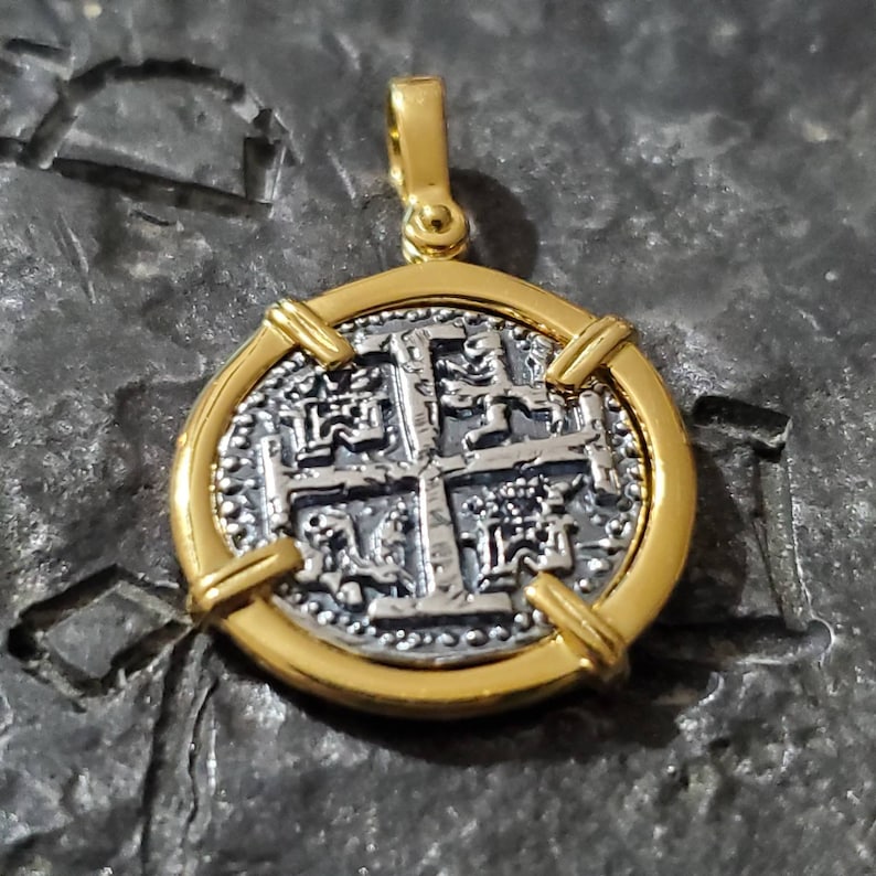 Pu&ograve; includere: Un ciondolo rotondo in oro e argento con una croce con dettagli intricati. Il ciondolo ha una superficie testurizzata.