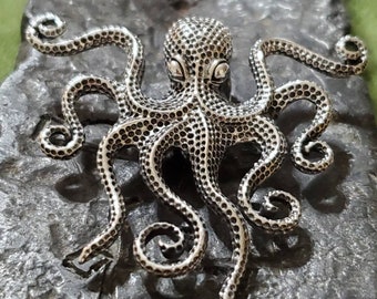 May include: A silver octopus sculpture with a textured, dotted surface. The octopus has eight tentacles that are curled and detailed.