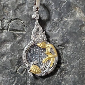 May include: Silver and gold pendant featuring a woman's figure with a crown of diamonds, holding a silver coin with a four-leaf clover design. The pendant is attached to a silver chain.