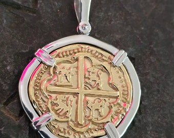 May include: A gold and silver pendant featuring a replica of a Spanish gold coin with a cross and four shields. The coin is surrounded by a silver frame.