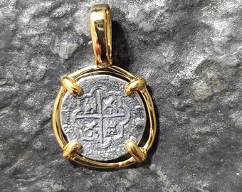 Op de afbeelding: Een zilveren munt hanger met een gouden rand en een kruisontwerp. De munt heeft een verhoogde rand en een lus aan de bovenkant om op te hangen.