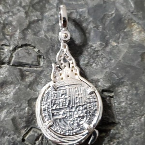 May include: Silver pendant featuring a detailed replica of a Spanish colonial coin with a decorative flame design on the bail.