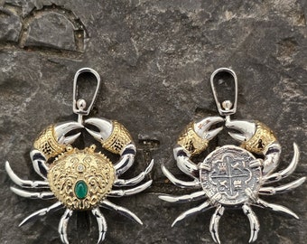 May include: Two-sided silver crab pendant with gold accents. One side features a green gemstone and intricate details, while the other side has a silver coin with a cross design.