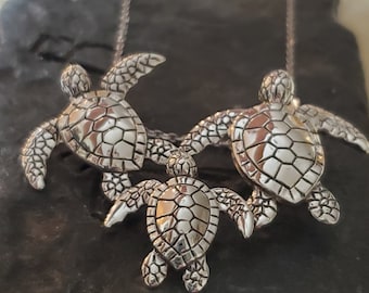 Può includere: Una collana d'argento con tre ciondoli a forma di tartaruga. Le tartarughe sono disposte a cascata, con la più grande in alto e la più piccola in basso.