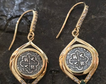 Könnte beinhalten: Goldene Ohrringe mit einem silbernen Münzenanhänger mit einem Kleeblatt-Design. Die Ohrringe haben eine diamantförmige Fassung mit einem grünen Edelstein an der Unterseite.