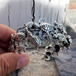 May include: Silver cuff bracelet featuring a design of multiple sea turtles, each with detailed textured shells.