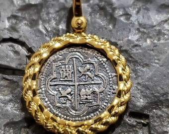 May include: A gold-plated pendant featuring a silver coin with a detailed design of four shields. The coin is surrounded by a rope-like gold border.