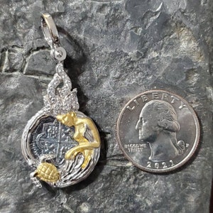 May include: Silver and gold pendant featuring a mermaid with a pearl crown, holding a silver coin with a cross design. The pendant is surrounded by a silver wave design and a gold turtle.